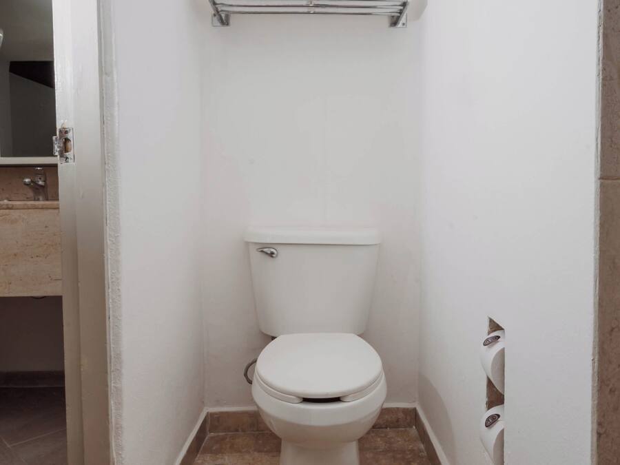 A small, white bathroom with a toilet, a towel dispenser, and a mirror.