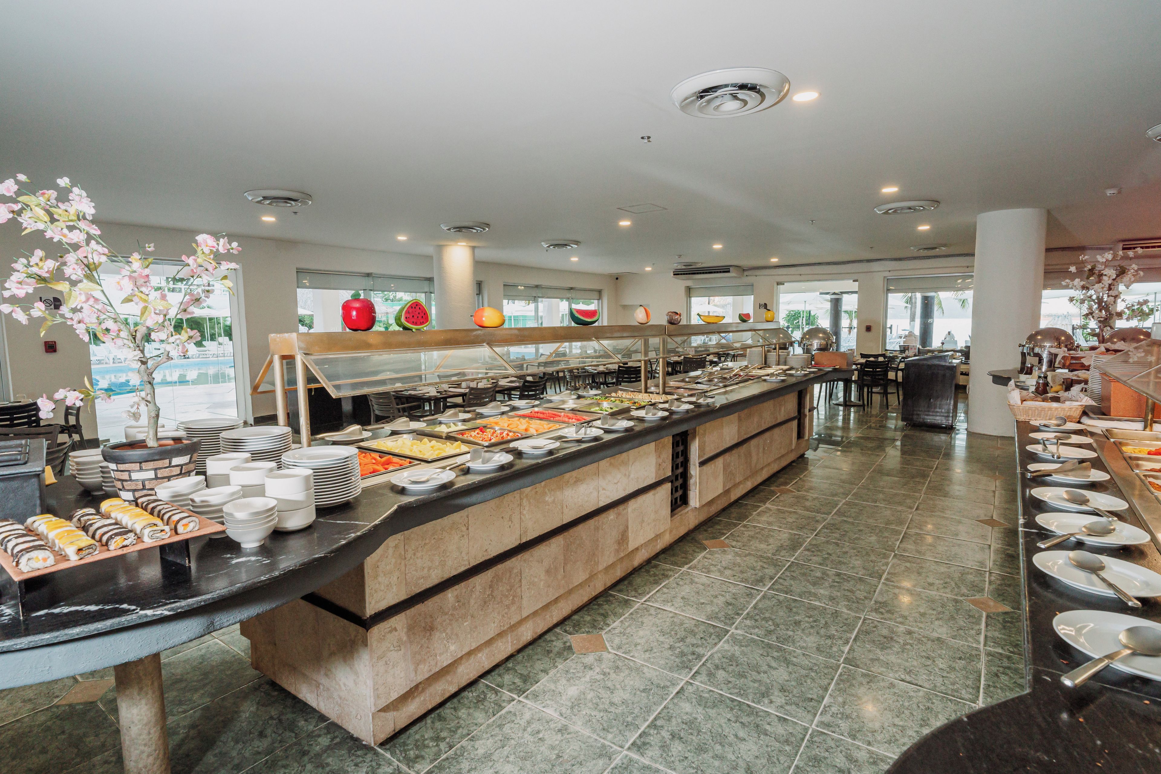 A buffet area with a variety of food options, a seating area with tables, and a view of the outdoors through large windows.