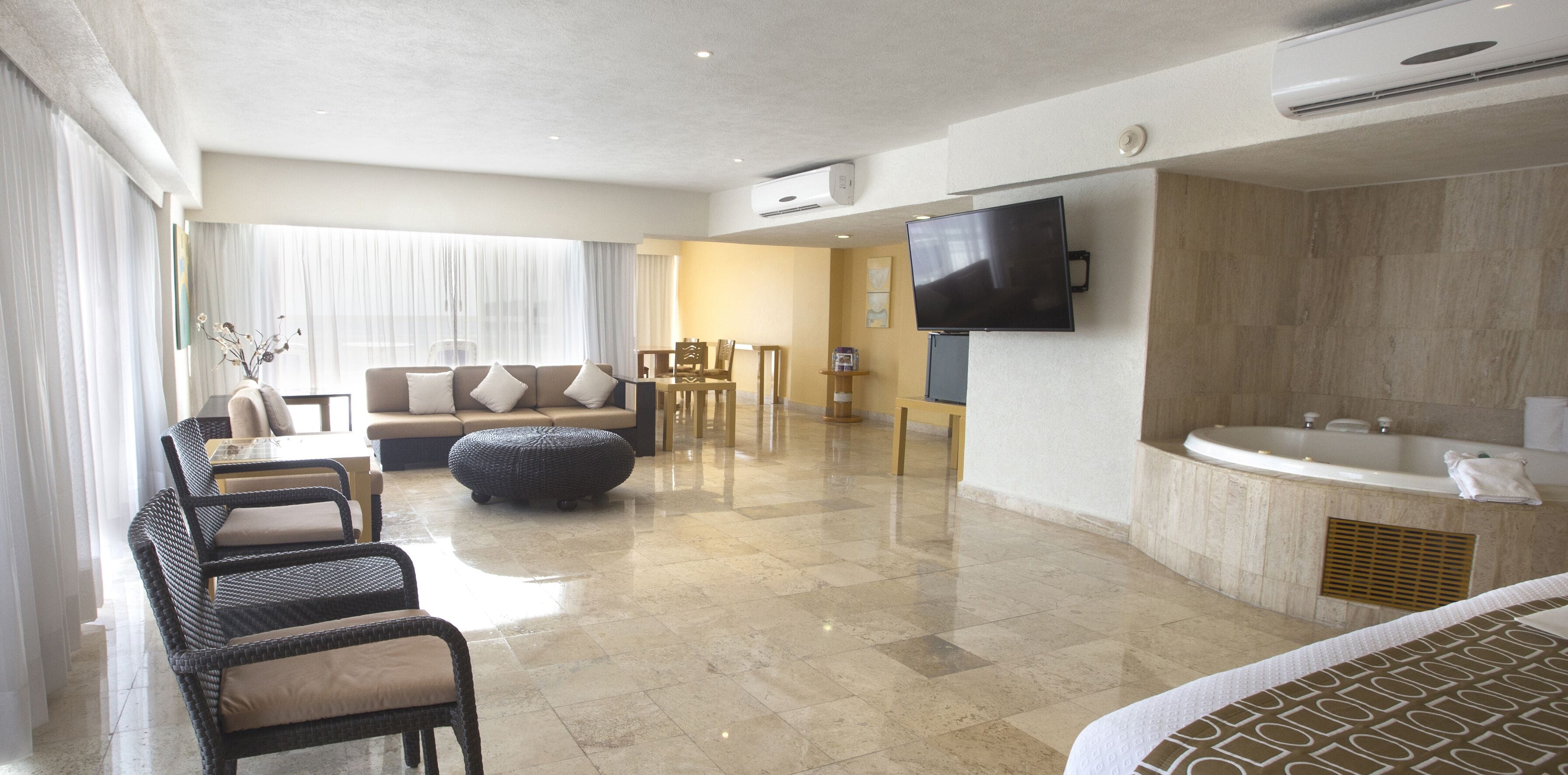 Ein modernes Hotelzimmer mit einer Sitzecke, Hocker und einem an der Wand befestigten Flachbildfernseher.