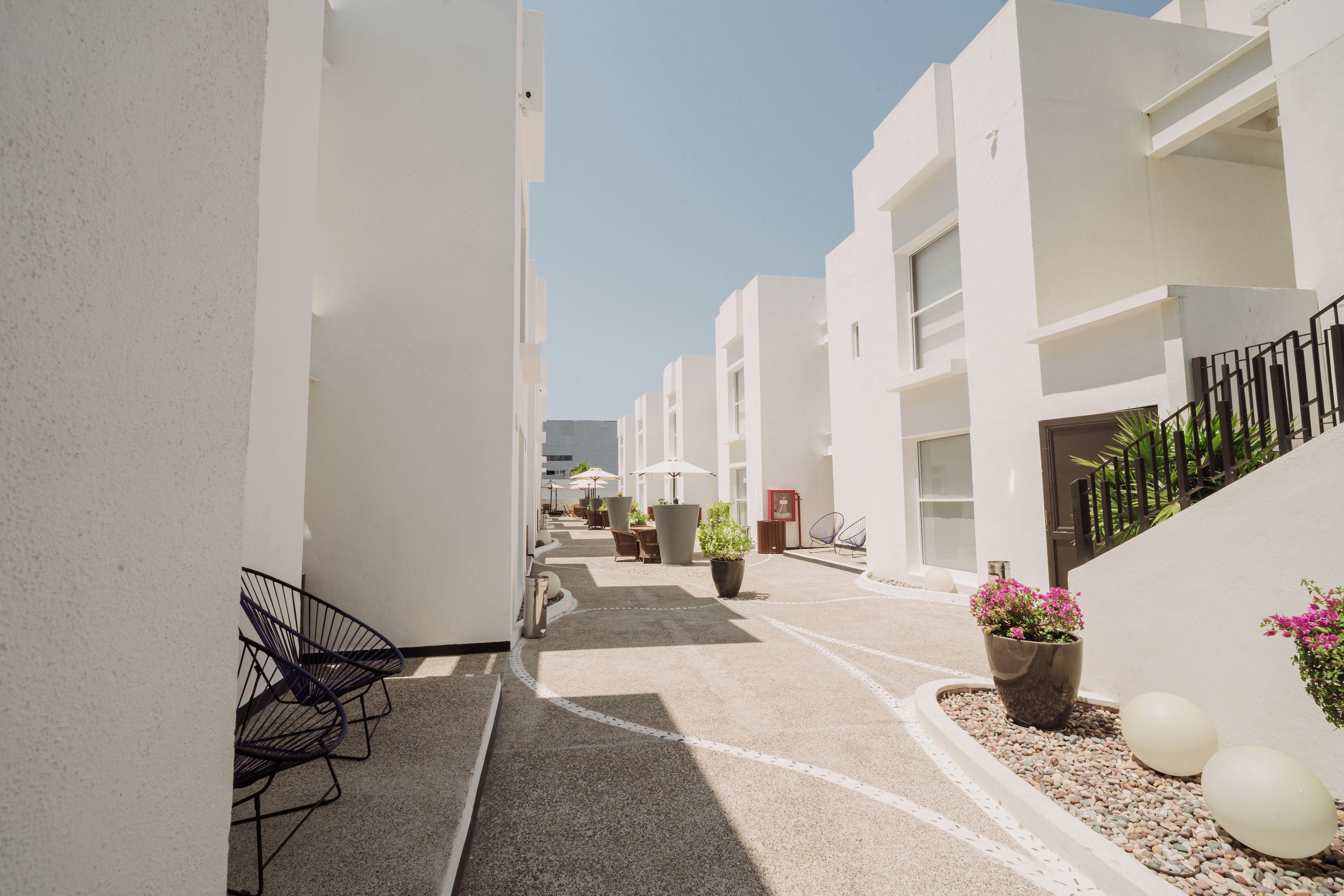 A narrow pathway between white buildings with outdoor seating and potted plants.