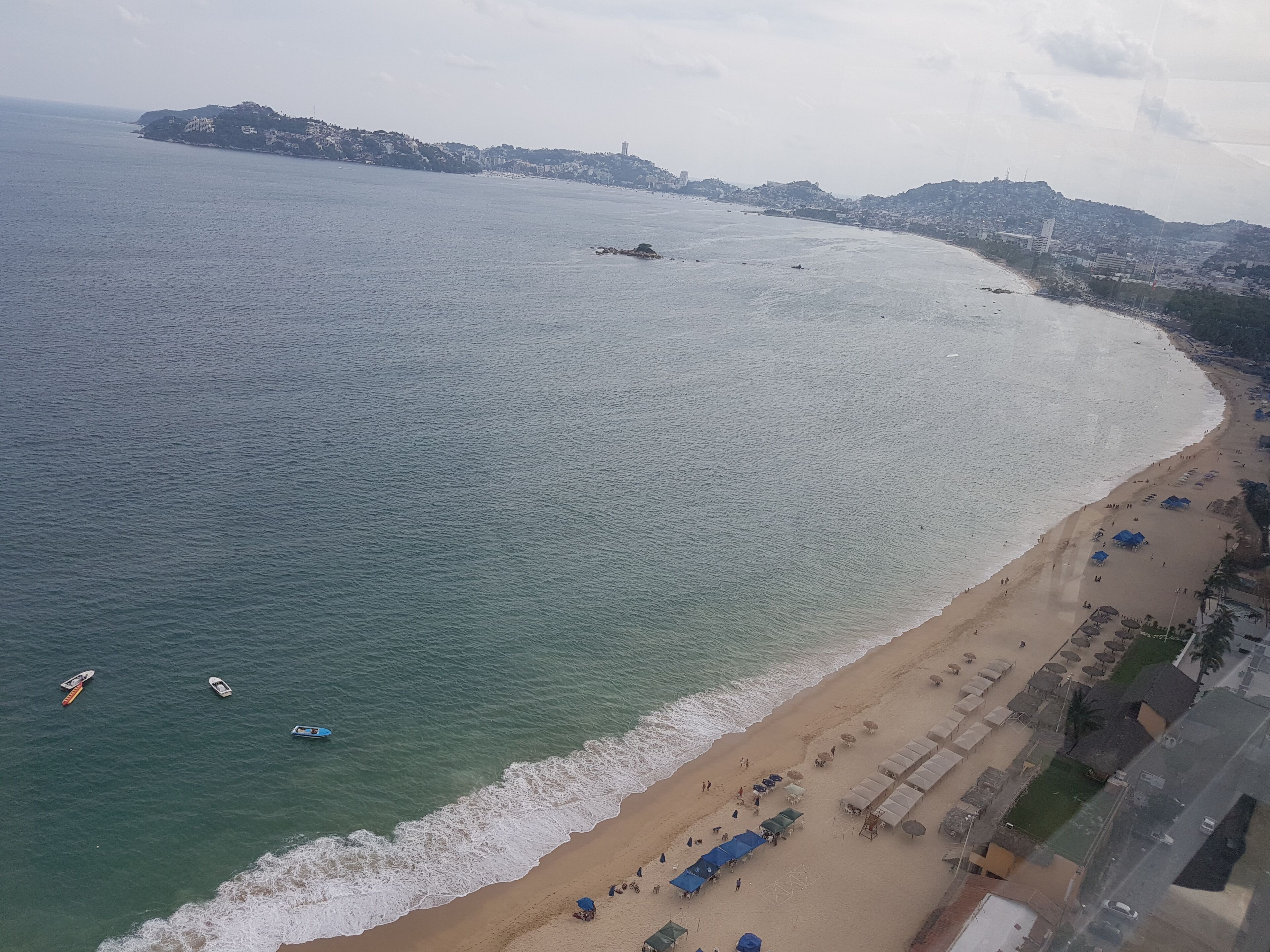 A coastal beach with a sandy shore, a few boats, and a cityscape in the background.