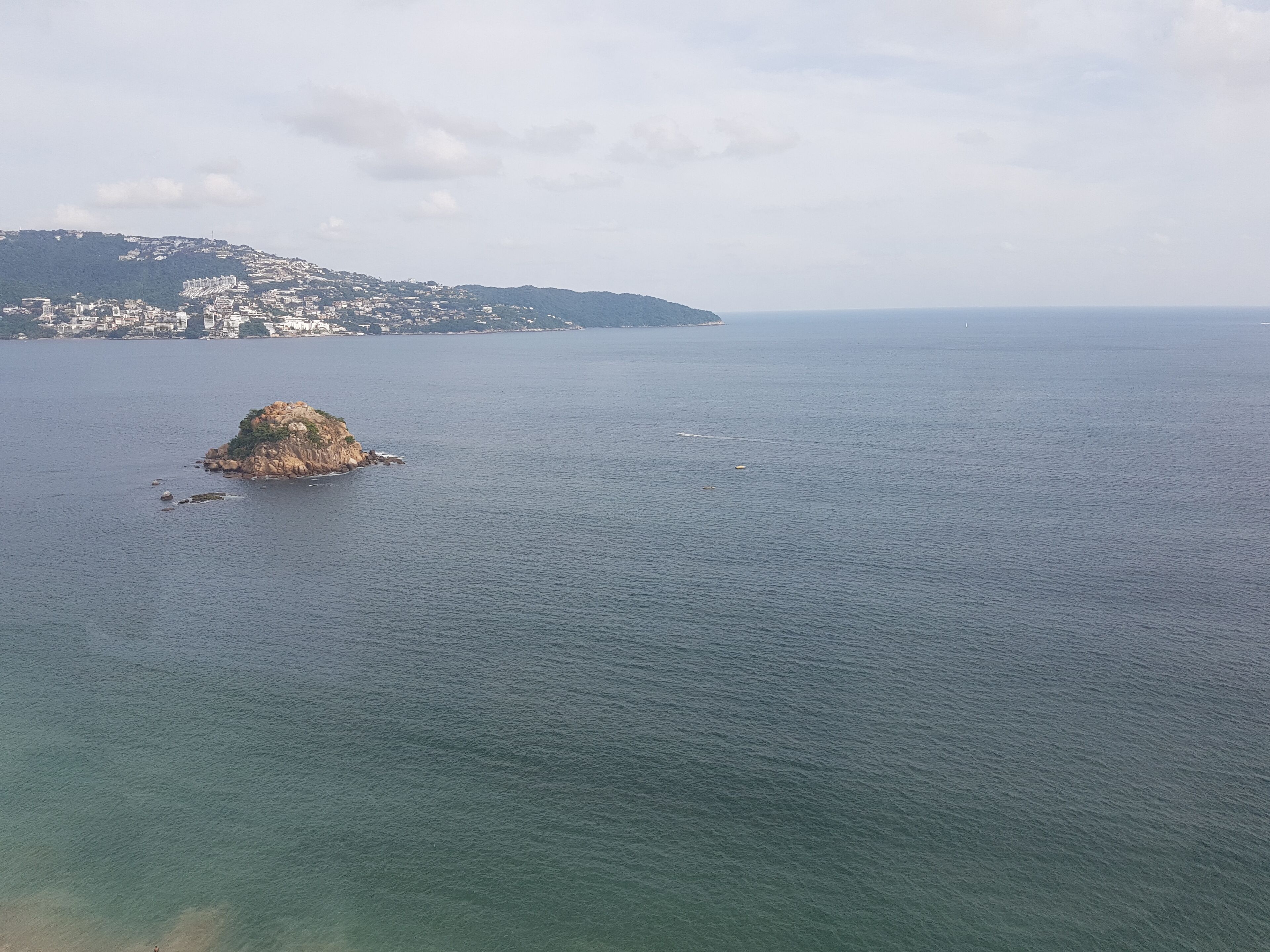 A coastal view with a small rocky island and a distant cityscape.