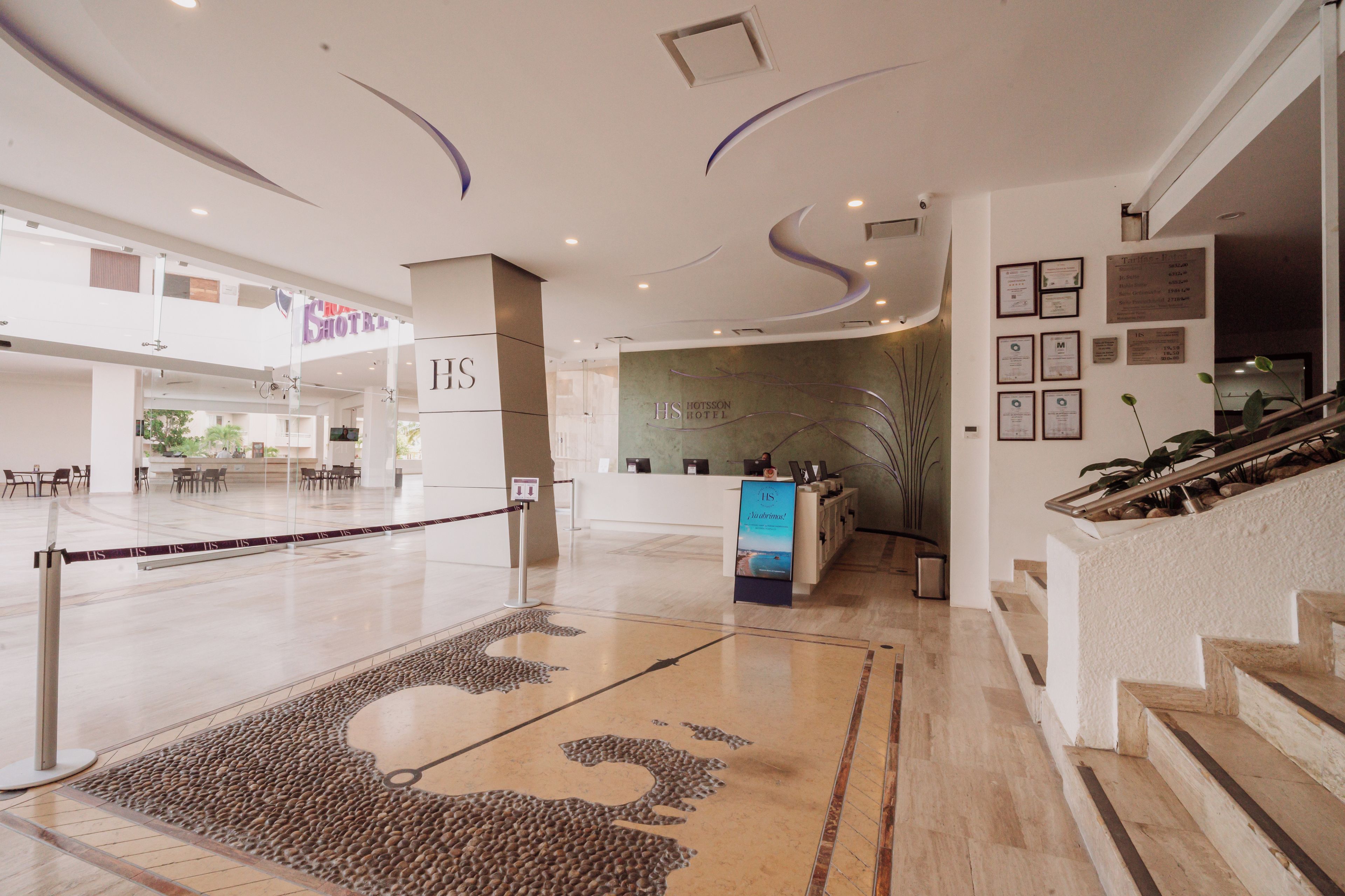 A hotel lobby with a reception desk, a staircase, and a large decorative rug.