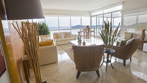 Amplia sala de estar con un gran ventanal que ofrece una vista panorámica, amueblada con sofás blancos, sillones de mimbre y una mesa de centro.