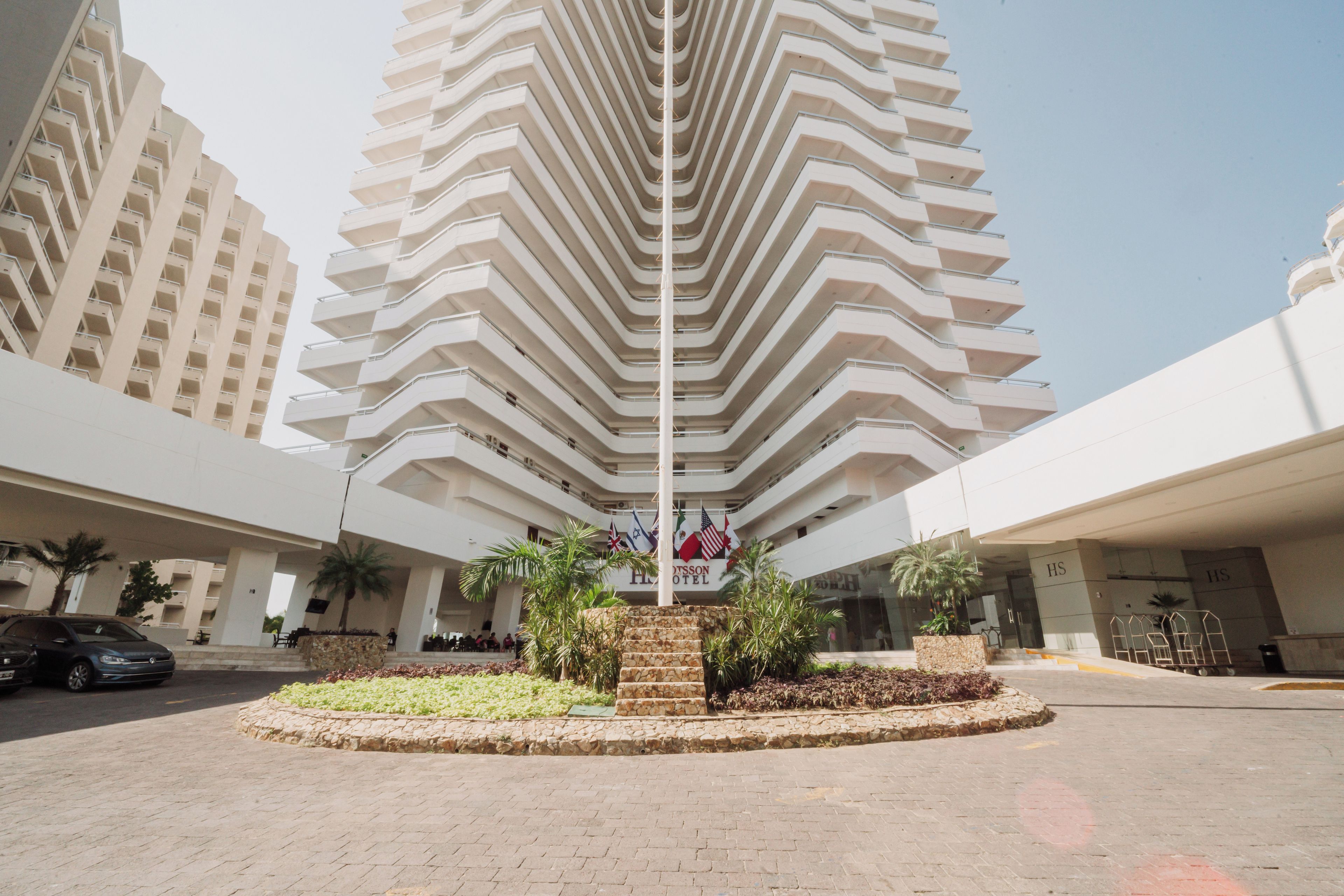 A hotel entrance with a modern design, featuring a central staircase surrounded by greenery and a stone wall.