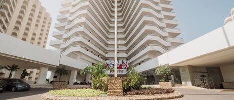 A hotel entrance with a modern design, featuring a central staircase surrounded by greenery and a stone wall.