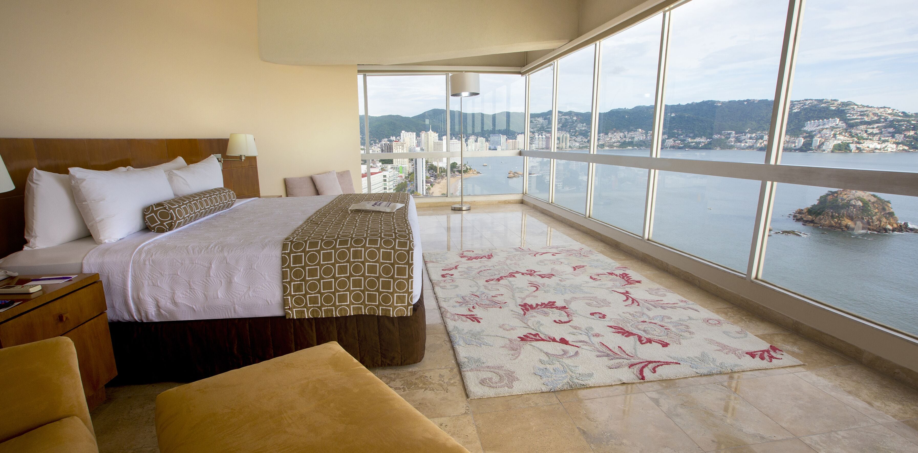 Habitación de hotel con una cama grande, vistas a la ciudad y al agua, y un balcón con vistas.