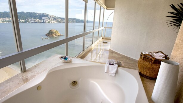 Un baño con una bañera grande, vista al mar y una cesta de mimbre.