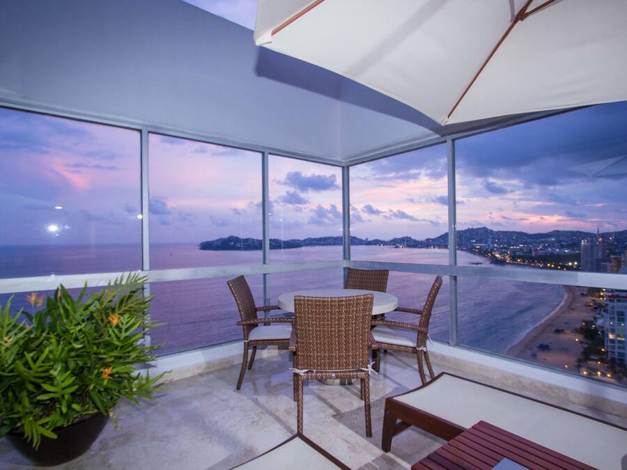 Uma varanda com vista para a praia e o horizonte urbano ao entardecer.