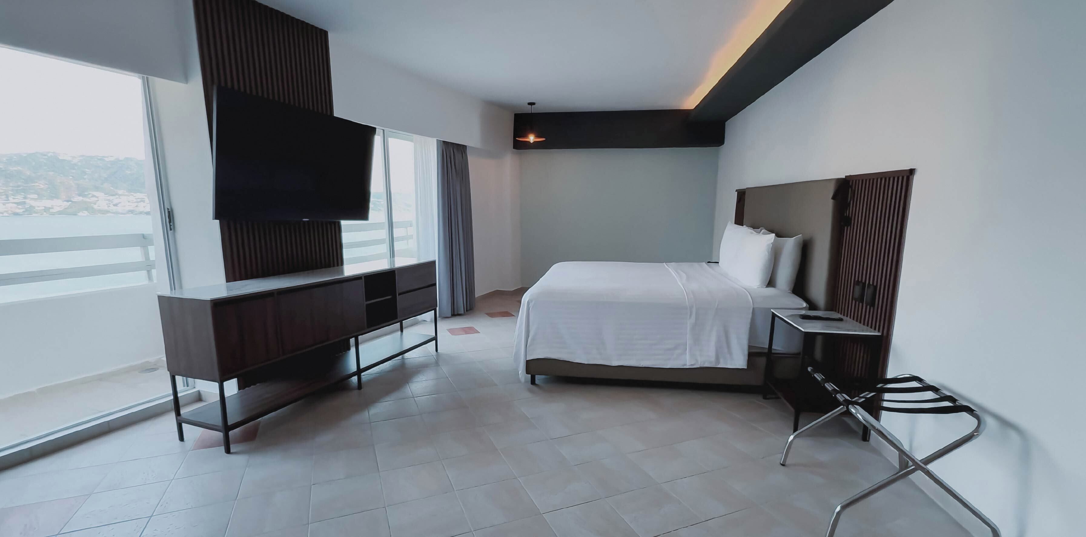 A modern hotel room with a bed, a TV, a desk, and a balcony with a view.