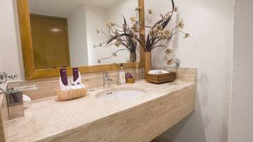 A bathroom with a marble sink, a mirror, a vase with dried flowers, and a basket with toiletries.