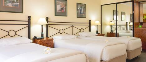 A hotel room with three single beds, each with a bedside table and lamp, and framed pictures on the wall.