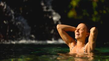 Una persona descansando en una piscina con una cascada al fondo.