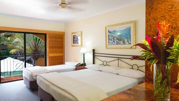 A hotel room with two beds, a balcony with a view, a painting on the wall, and a vase with flowers.