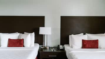 Quarto de hotel com duas camas, mesa de cabeceira com abajur e telefone, e um travesseiro vermelho em cada cama.