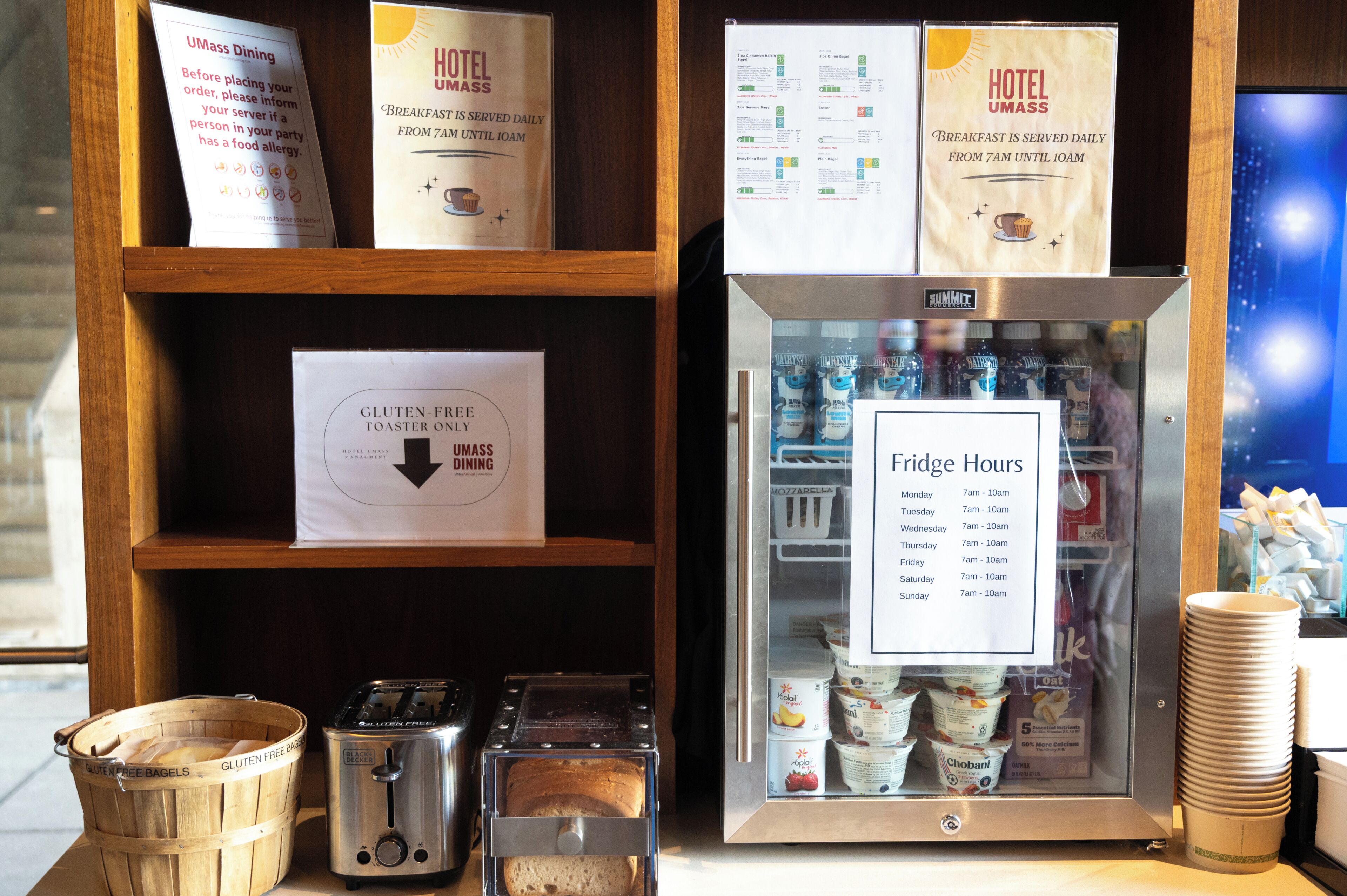 Zona de desayuno de hotel con opciones sin gluten, un refrigerador con horario de uso y un tostador.