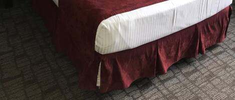Una habitación de hotel con una cama grande, cabecero negro, mesita de noche con lámpara y ventana con cortinas.