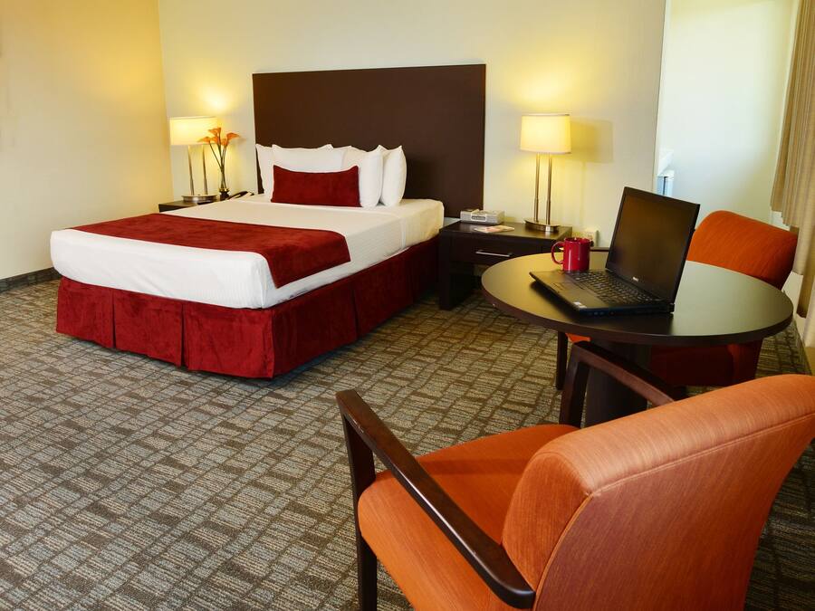 Ein Hotelzimmer mit Bett, Schreibtisch, Laptop, Stuhl und Lampe.