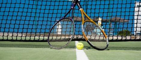 A tennis court with a net, two tennis rackets, and a tennis ball.
