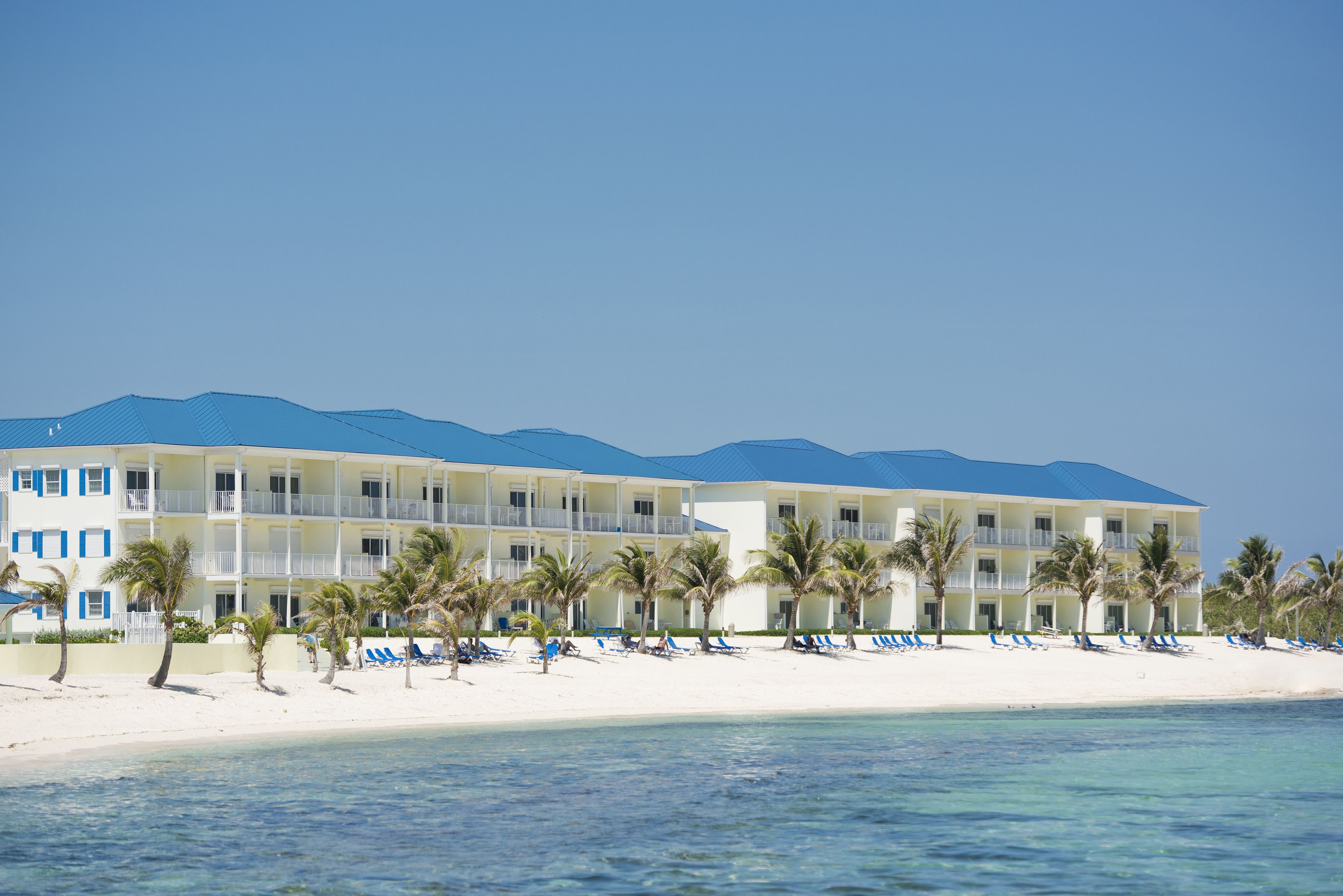 A beachfront hotel with multiple balconies, palm trees, and beach chairs.