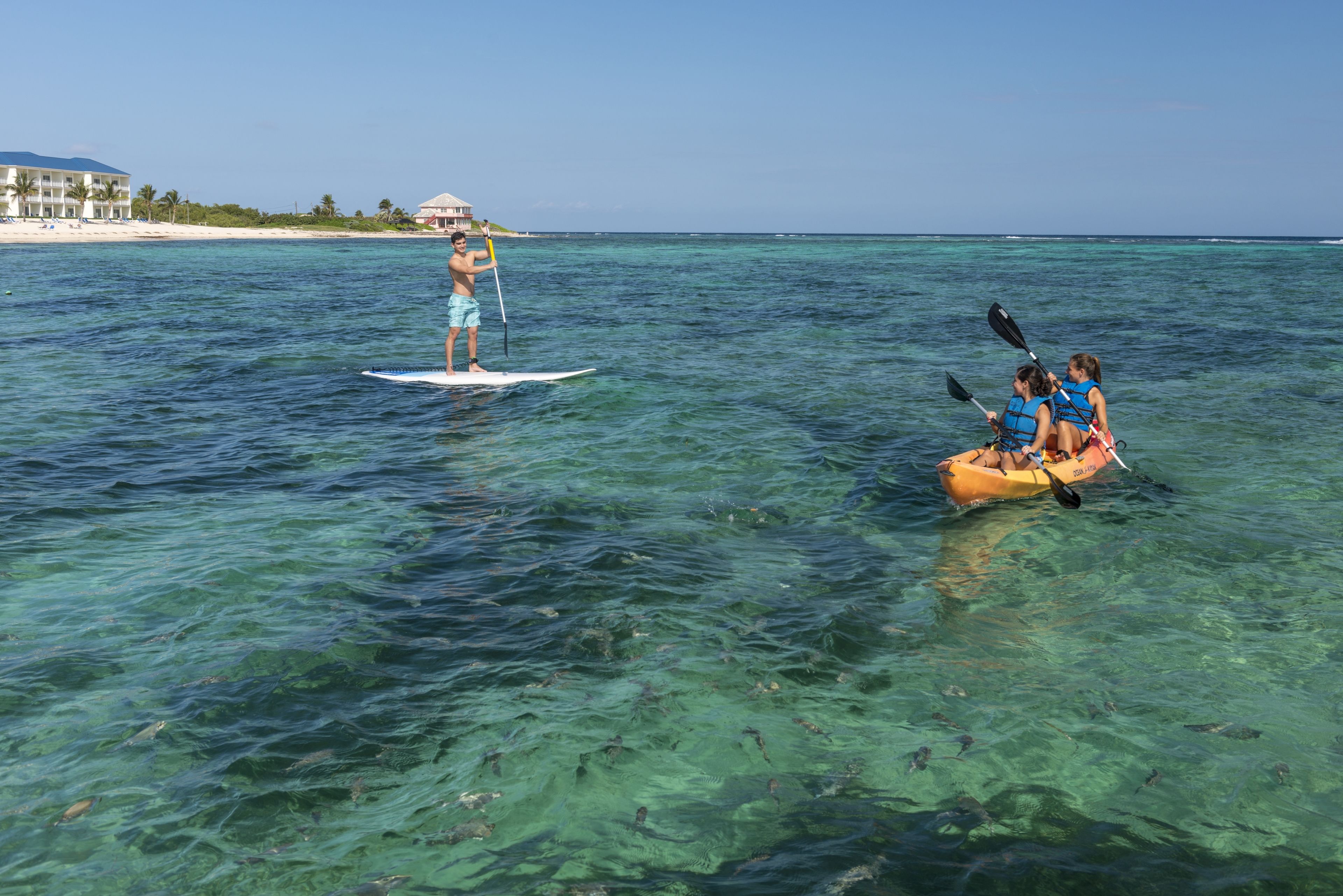 Helder tropisch water met een persoon op een paddleboard en een groep die kajakt.