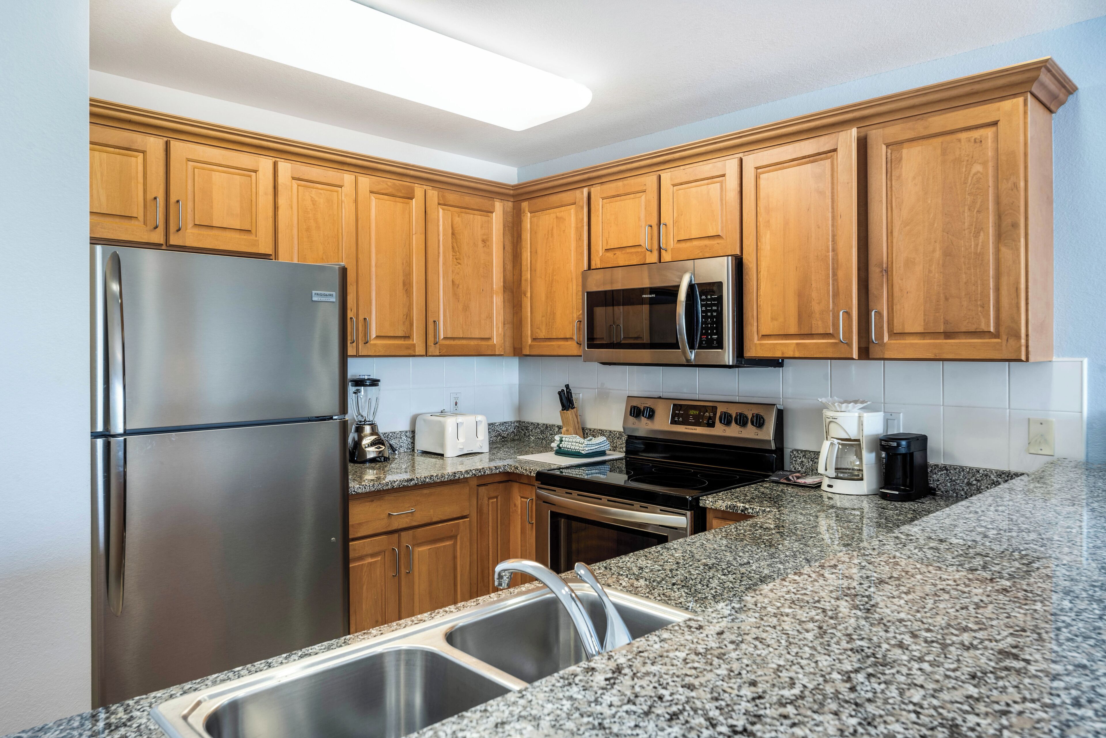 A modern kitchen with stainless steel appliances, wooden cabinets, granite countertops, and a built-in oven.