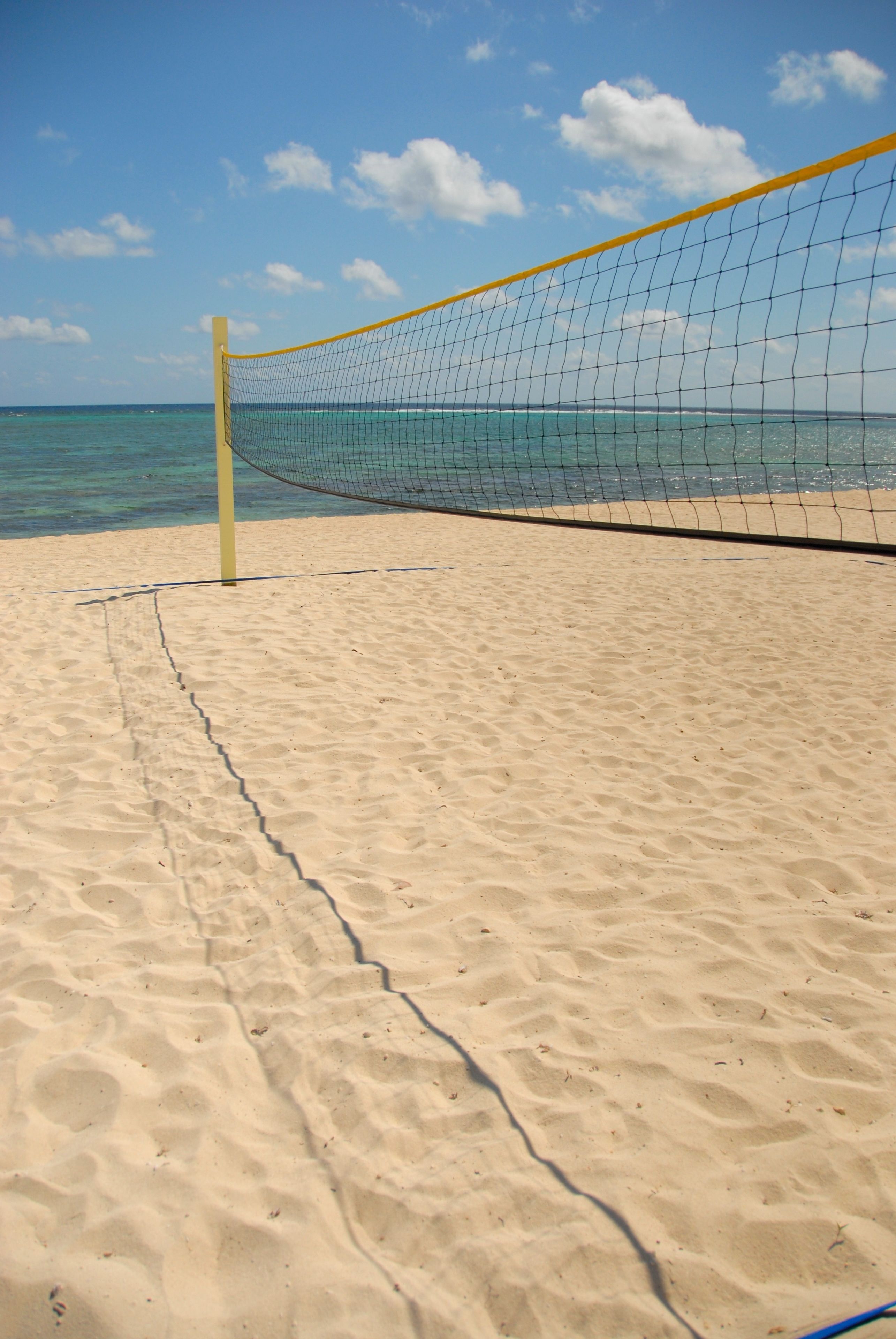 Una red de voleibol de playa sobre arena, con cielos despejados y agua tranquila al fondo.