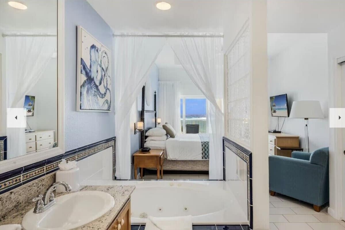 A modern bathroom with a bathtub, a large mirror, and a bed with a view of the sea.