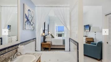 Un baño moderno con bañera, un espejo grande y una cama con vistas al mar.