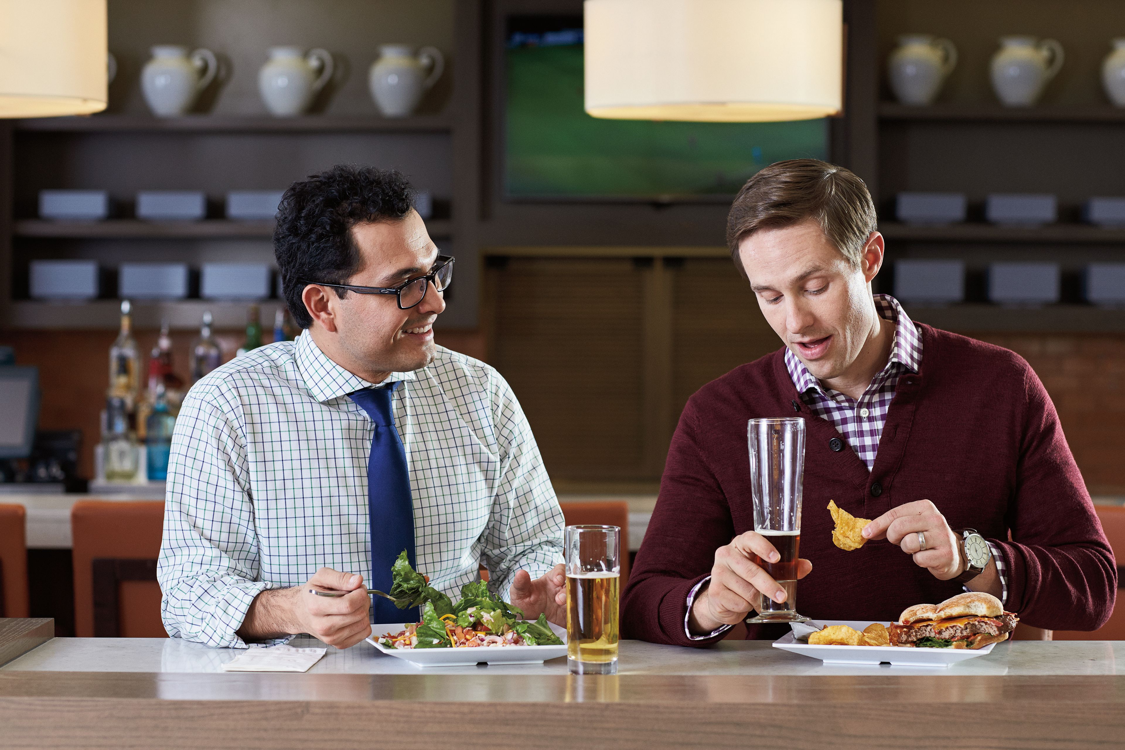 Deux hommes sont assis à une table dans un restaurant, devant des assiettes de nourriture et des boissons.