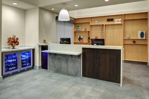 A reception area with a counter, shelves, a refrigerator, and a hanging light fixture.