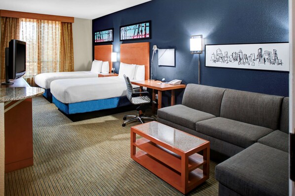 A hotel room with two beds, a sofa, a desk, and a TV.