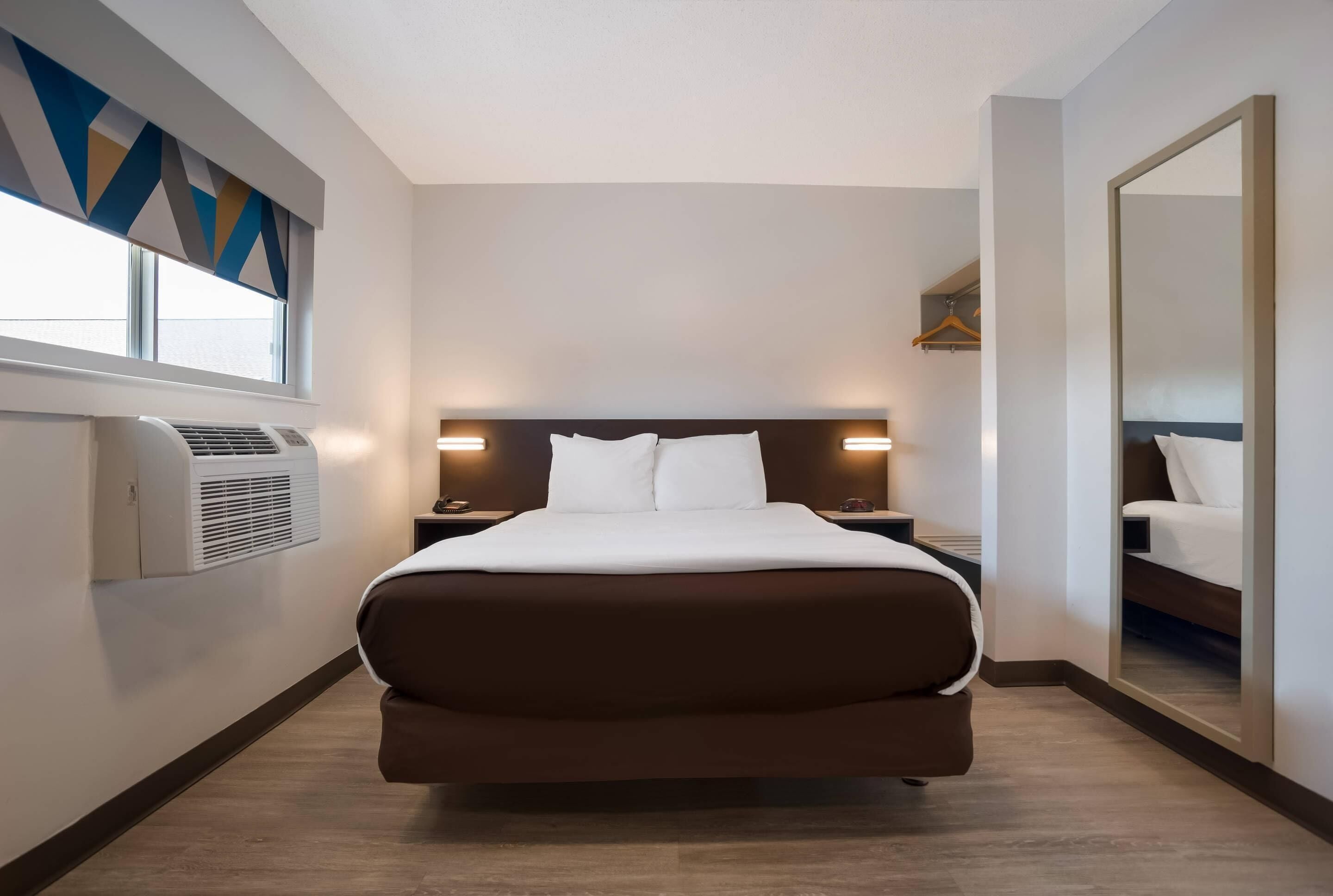 A modern hotel room with a large bed, bedside lamps, a wardrobe, and a large mirror.