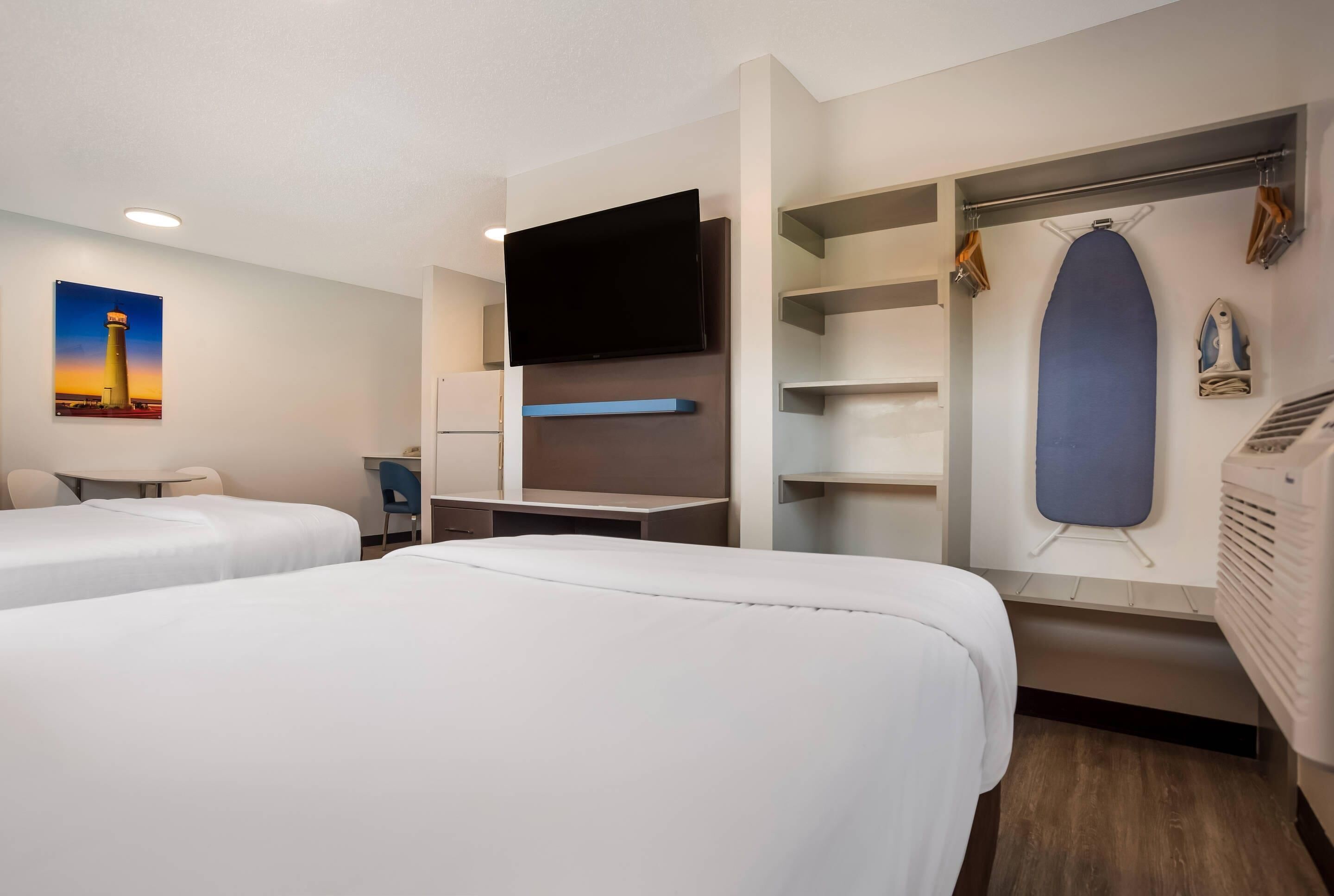 Een hotelkamer met twee bedden, een flatscreen televisie, een bureau, een stoel, een kledingkast en een poster aan de muur.