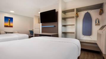 Een hotelkamer met twee bedden, een flatscreen televisie, een bureau, een stoel, een kledingkast en een poster aan de muur.