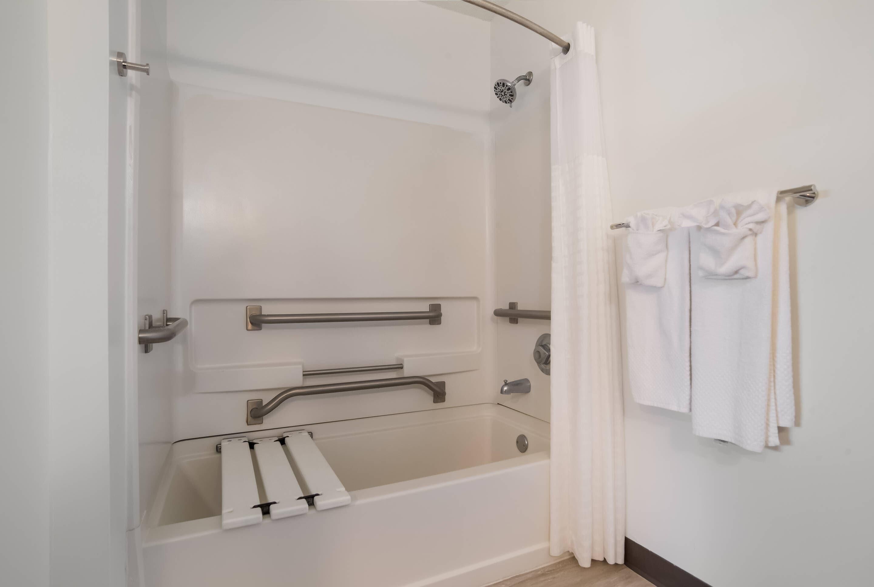 Une douche à l’italienne équipée de barres d’appui, d’une porte en verre et d’un porte-serviettes.