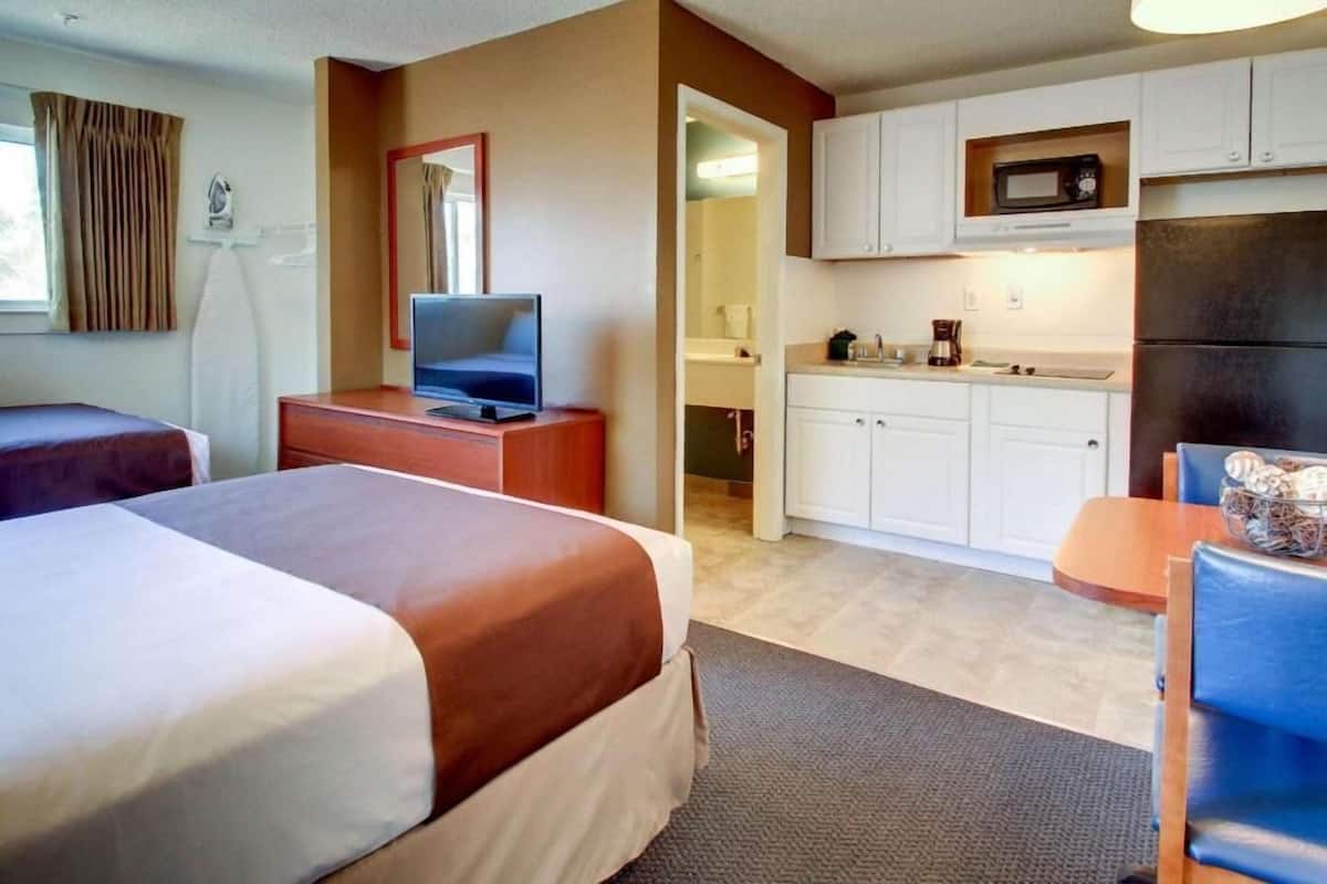 Ein Hotelzimmer mit zwei Betten, einem Fernseher, einer Küchenzeile und einem Badezimmer.