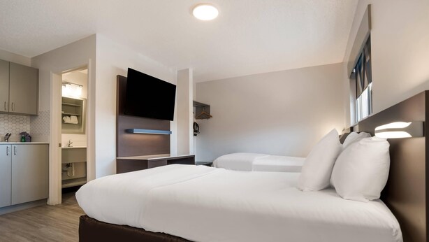 Une chambre d’hôtel moderne dotée d’un grand lit, d’un téléviseur à écran plat fixé au-dessus, d’un dressing et d’un petit coin cuisine.