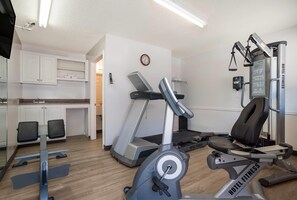 Gimnasio de hotel con cinta de correr, elíptica y banco de pesas.