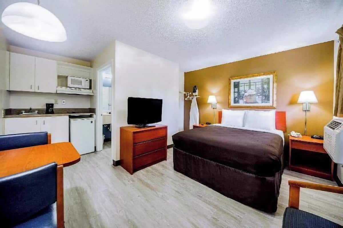 Ein Hotelzimmer mit Bett, Schreibtisch, Stuhl, Fernseher, Mikrowelle und einem Bild an der Wand.