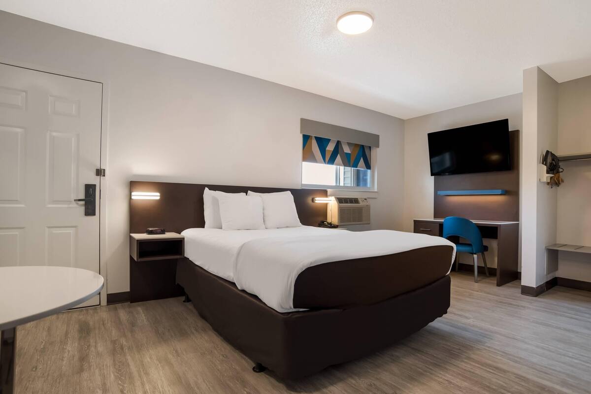 Ein Hotelzimmer mit Bett, Nachttisch, Schreibtisch, Stuhl, Fernseher und einem kleinen Fenster.