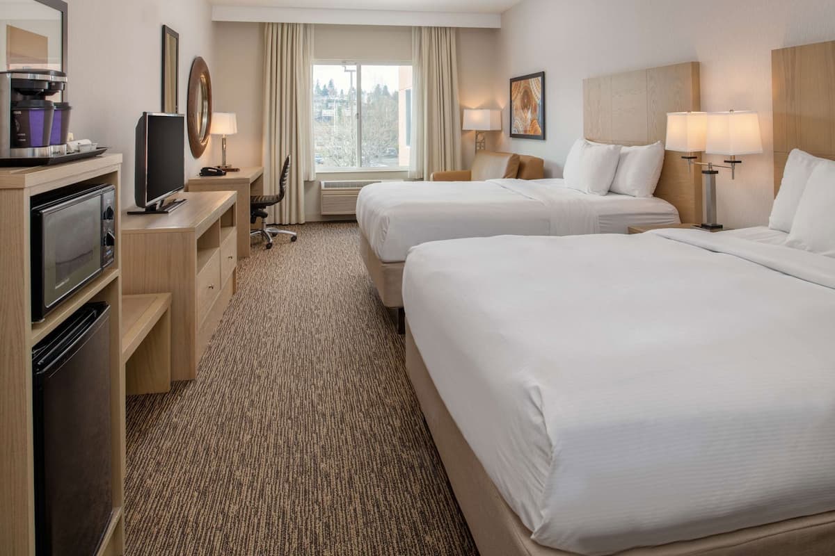 A hotel room with two beds, a desk with a television, a coffee maker, and a window with a view of the city.