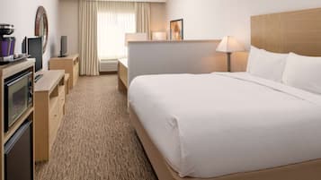 A hotel room with a large bed, a desk with a computer, a TV, and a minibar.