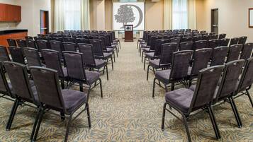 A conference room with rows of chairs facing a podium with a tree logo, a kitchen area, and a door.