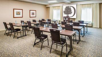 A conference room with a patterned carpet, multiple tables with chairs, framed pictures on the wall, and a projector screen with a tree image.