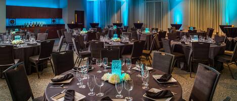 A banquet hall with round tables set for dining, a bar area, and a large window with curtains.