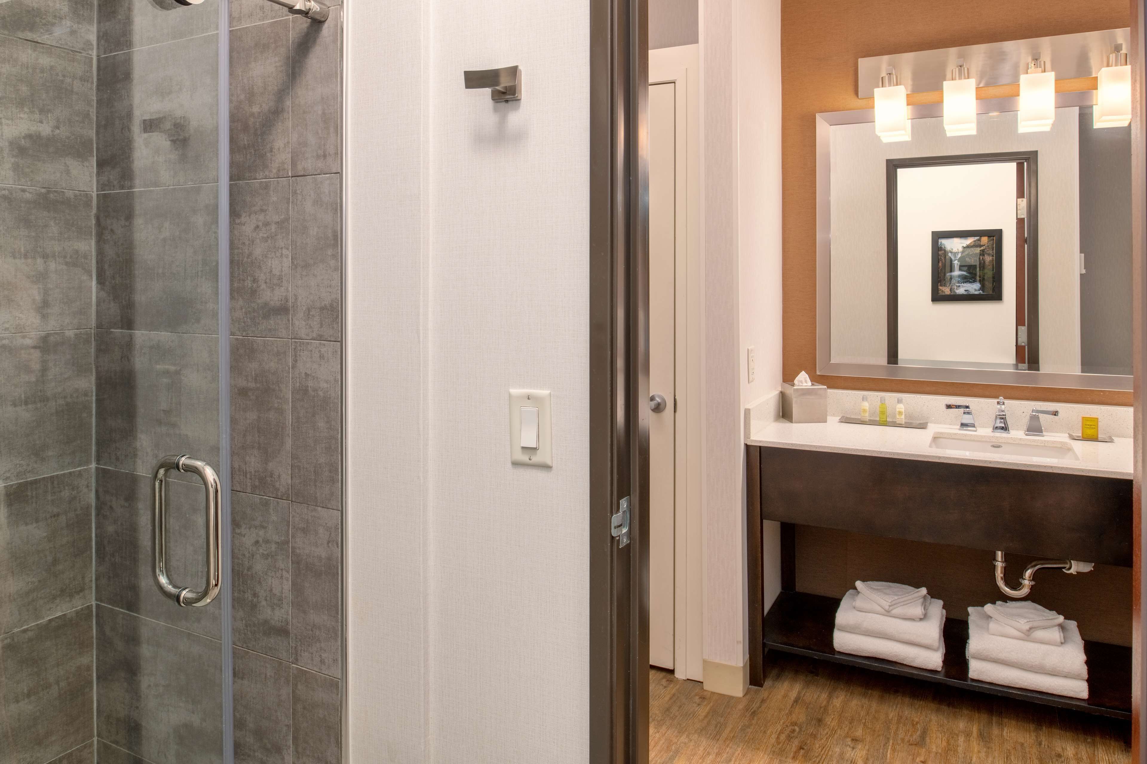 A modern bathroom with a glass shower enclosure, a vanity with a mirror, and neatly folded towels.