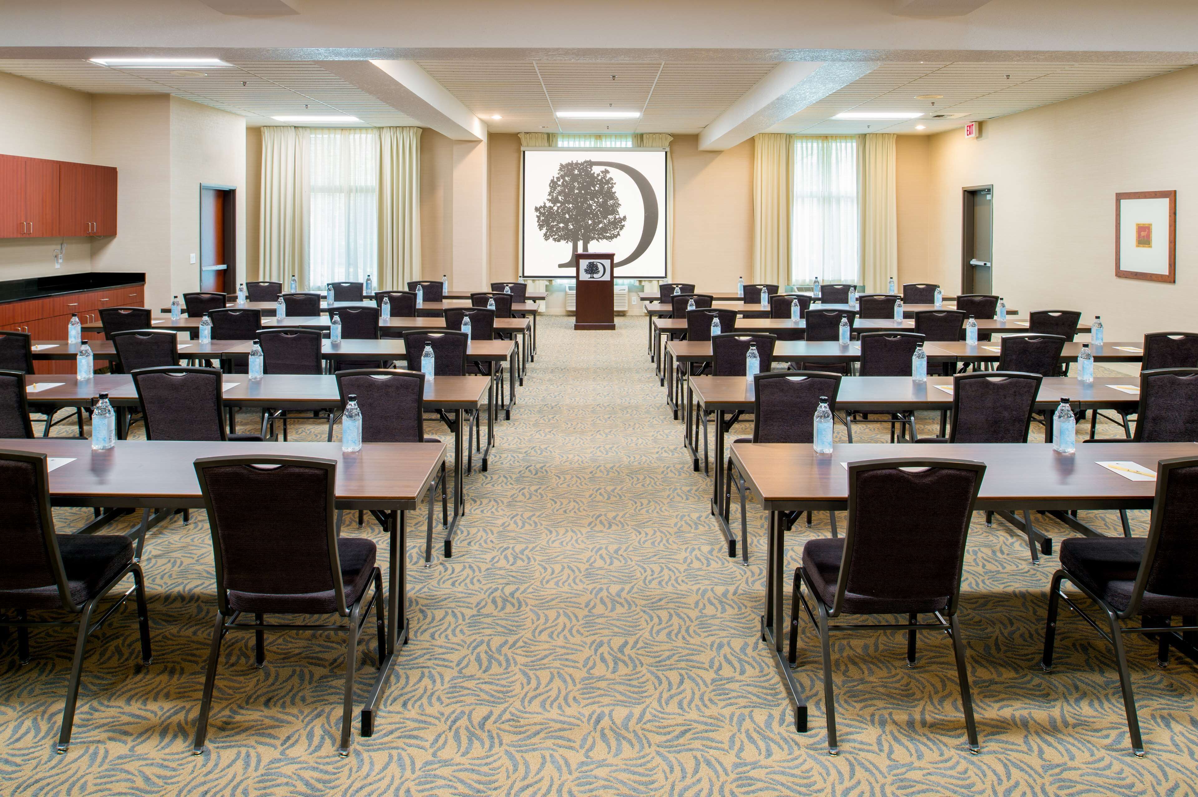 A conference room with rows of tables and chairs, a podium, and a projection screen displaying a tree.