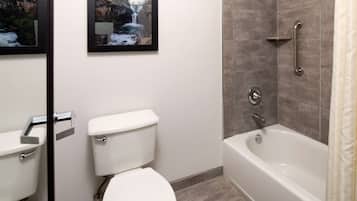 A bathroom with a toilet, a framed picture of a waterfall, a bathtub, and a shower with a grab bar.