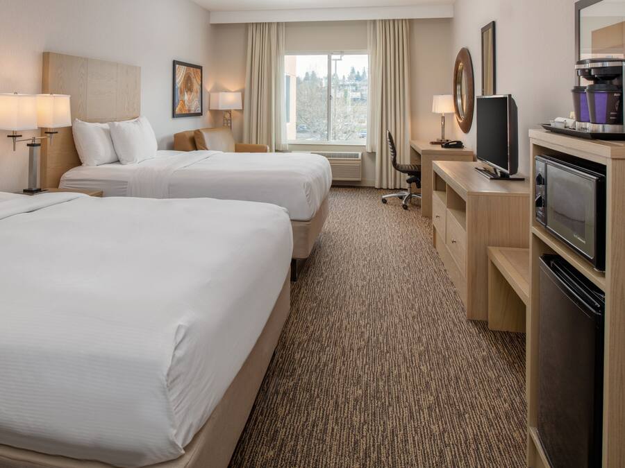 A hotel room with two beds, a desk with a television, a coffee machine, and a window with curtains.